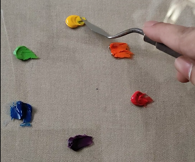 3 primary colors and 3 secondary color swatches are on the palette. yellow, orange, red, violate, blue and green oil color is on the palette. mixing with painting knife.